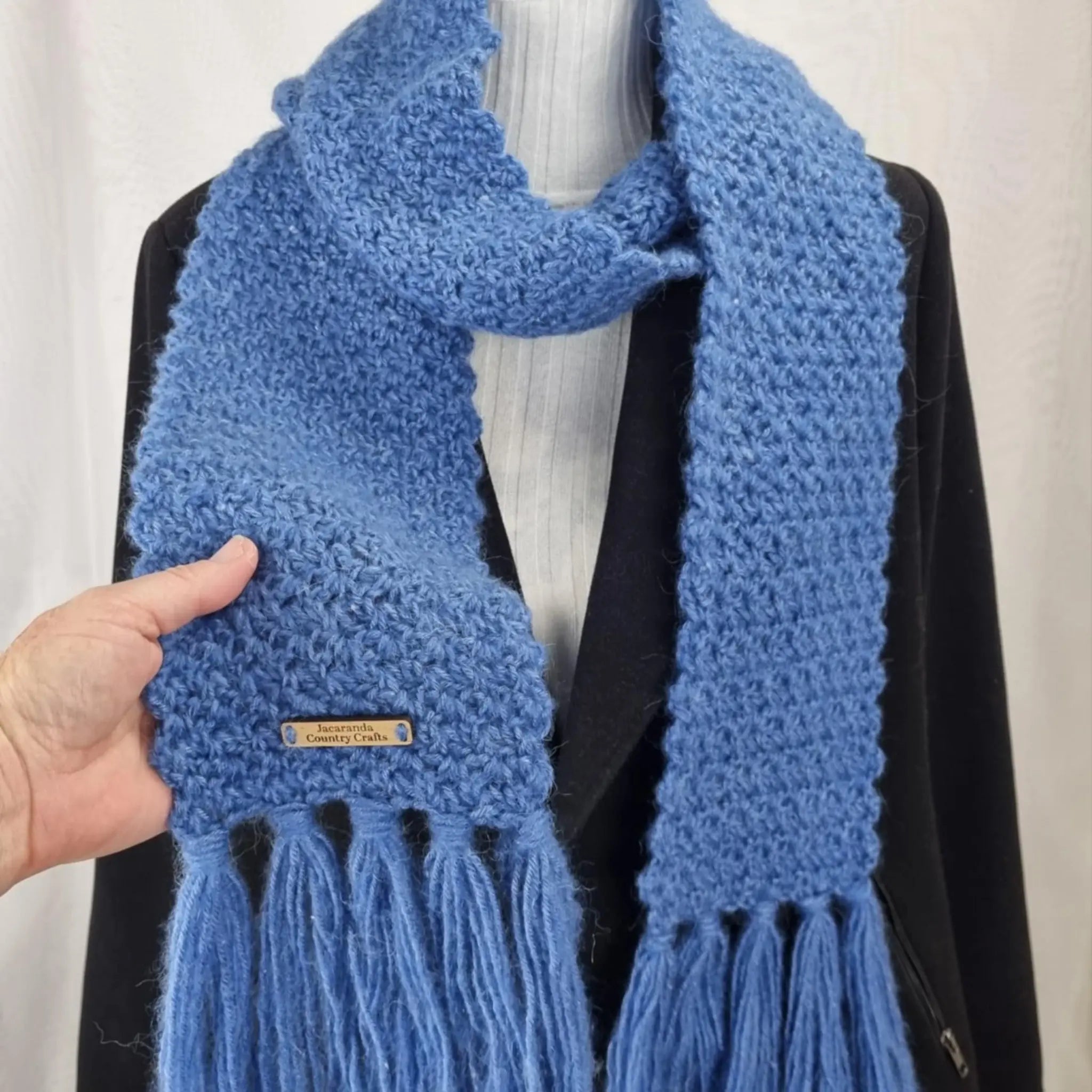 Blue knitted scarf with a brand tag on a mannequin against a white background Heirloom Cosy Blue Scarf