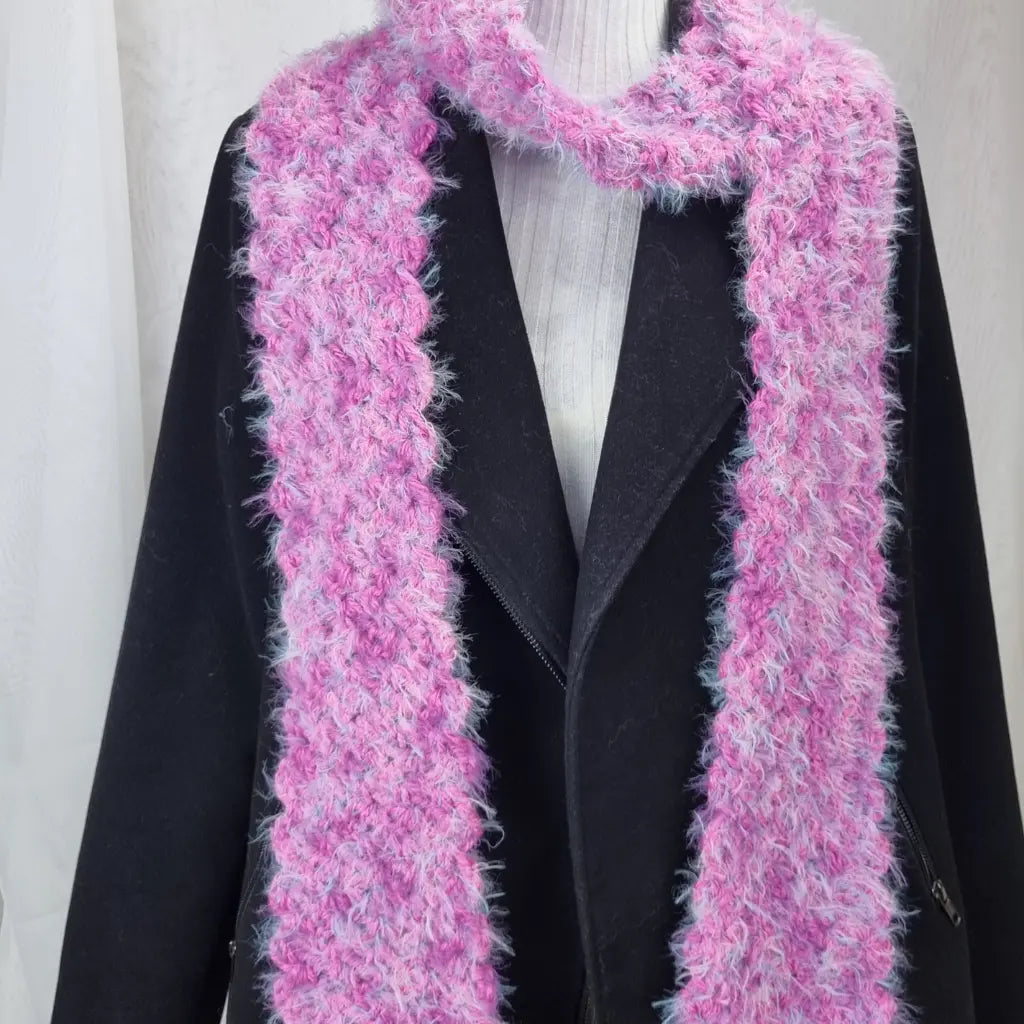 Pink knitted scarf draped over a black coat on a white background