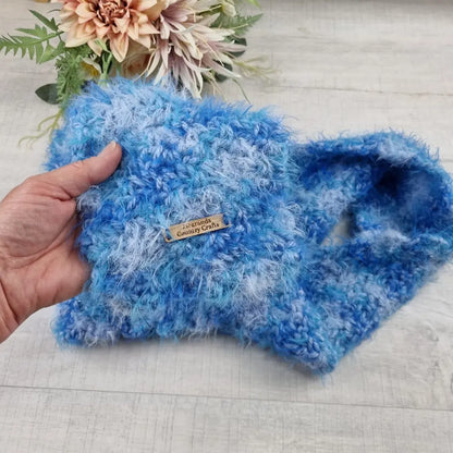 Blue textured fabric held by a hand with a 'Country Crafts' label, on a light wooden surface with flowers in the background.