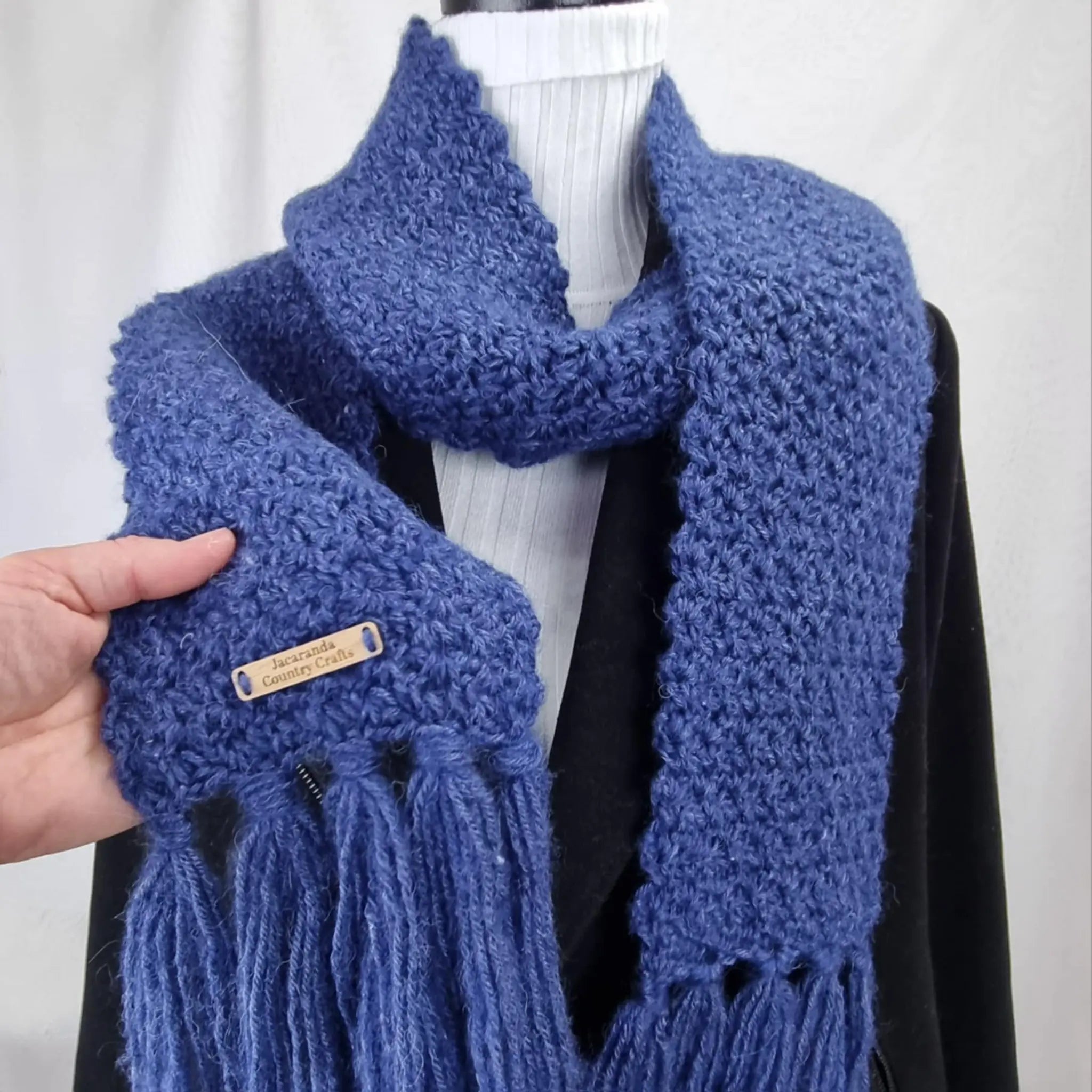 Blue knitted scarf with tassels held by a hand against a white background Heirloom Cosy Marlin Scarf Handmade